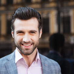 Close up portrait of a smiling handsome man in a jacket looking at camera in a city area